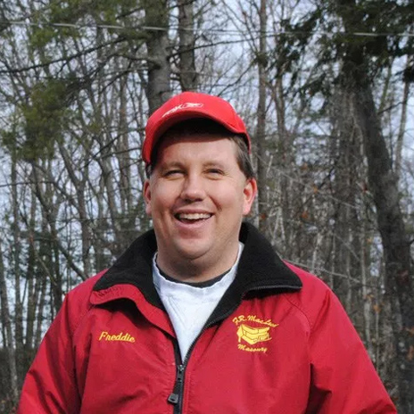 Man with red hat and jacket smiling in the woods